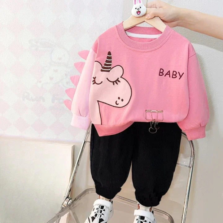 Pink sweater with cartoon design and black pants on a chair against a light background