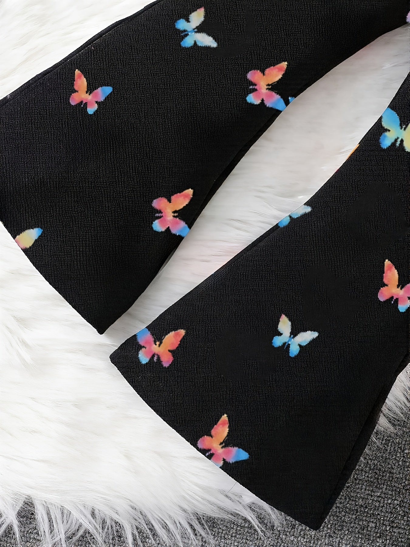 Black wide-leg pants featuring a colorful butterfly print, styled on a white faux fur rug.