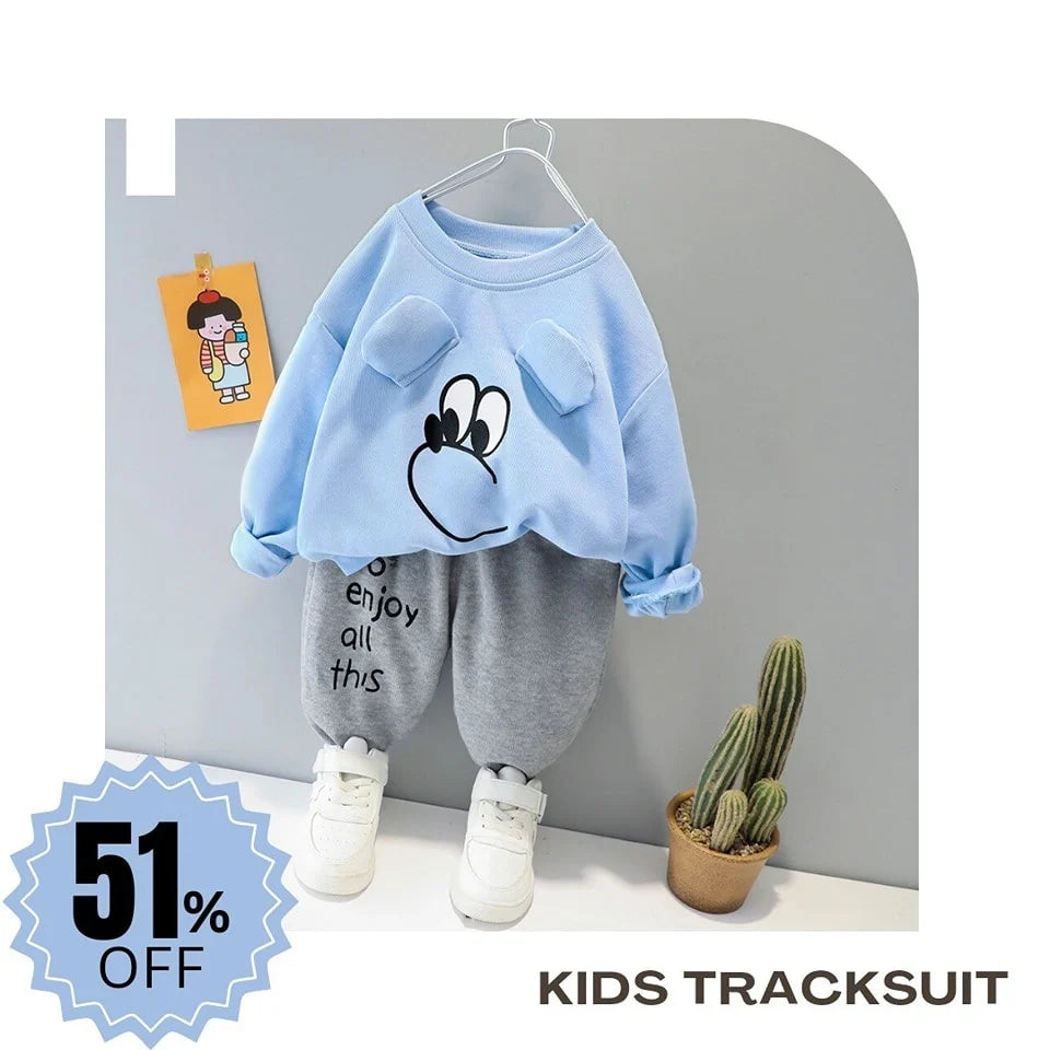 Children's tracksuit with a blue top and gray pants on a hanger against a gray wall.