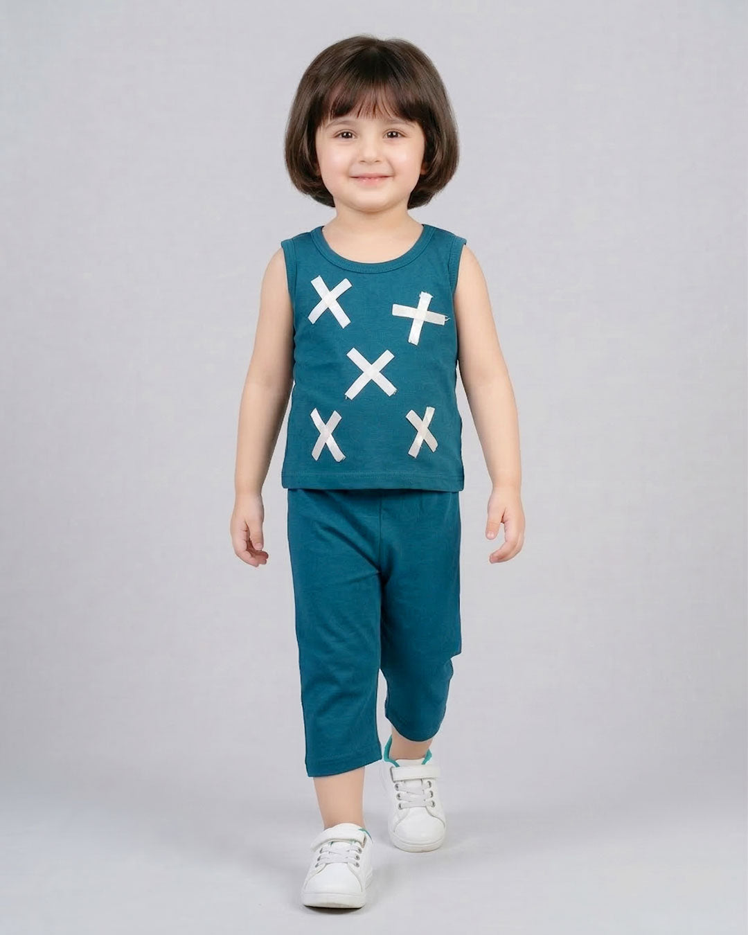 Child wearing a teal sleeveless top with white cross patterns and matching pants on a gray background