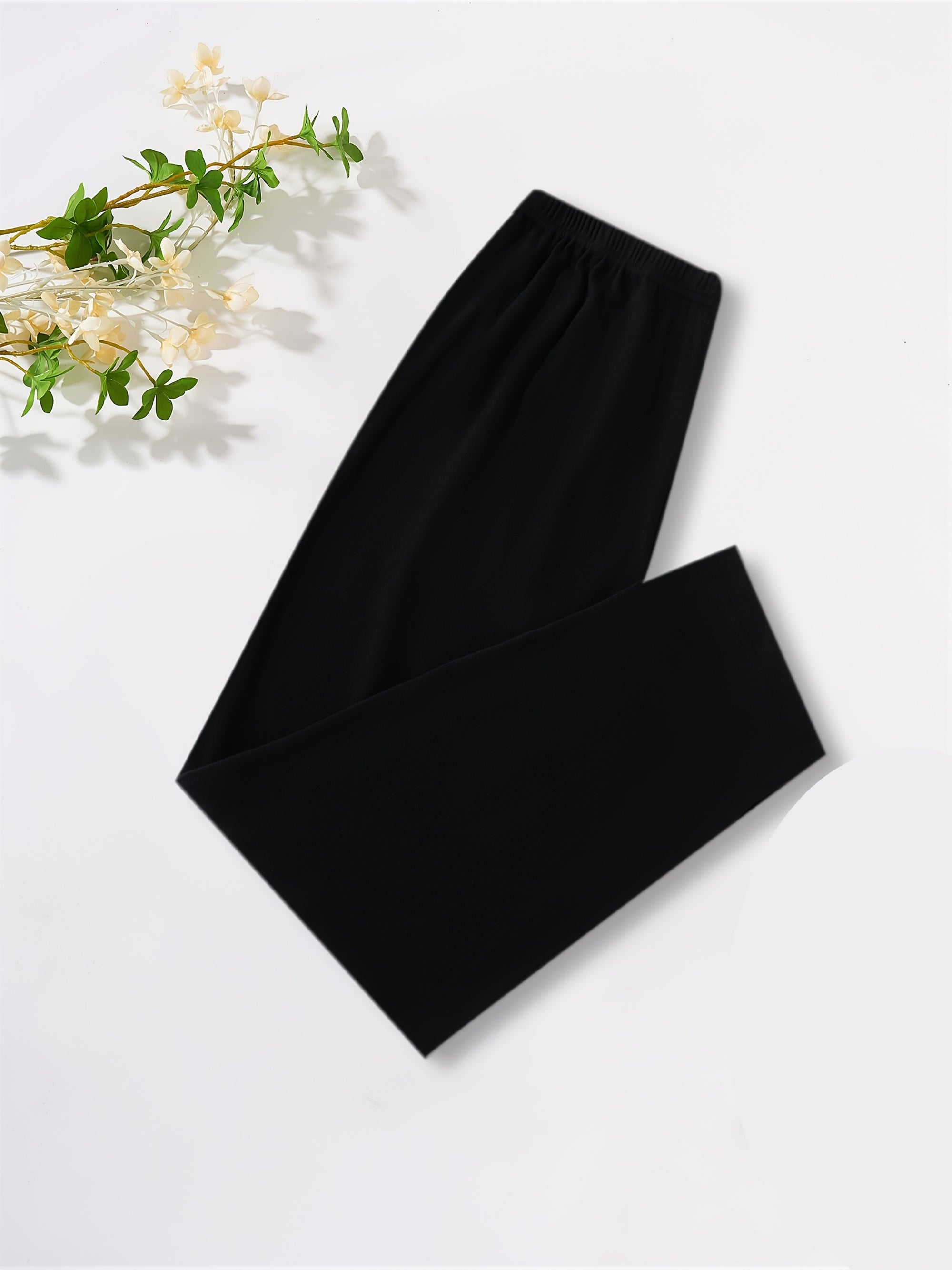 Black wide-leg lounge pants folded neatly on a white background with a decorative sprig of white flowers in the top-left corner.