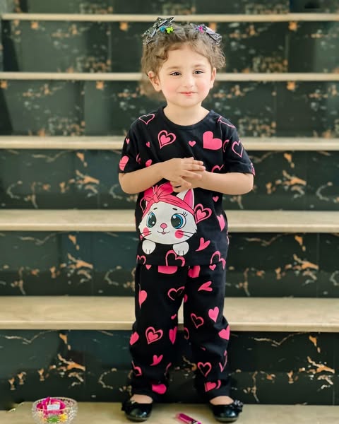 Child wearing a black outfit with pink hearts and a cartoon character, standing on steps.