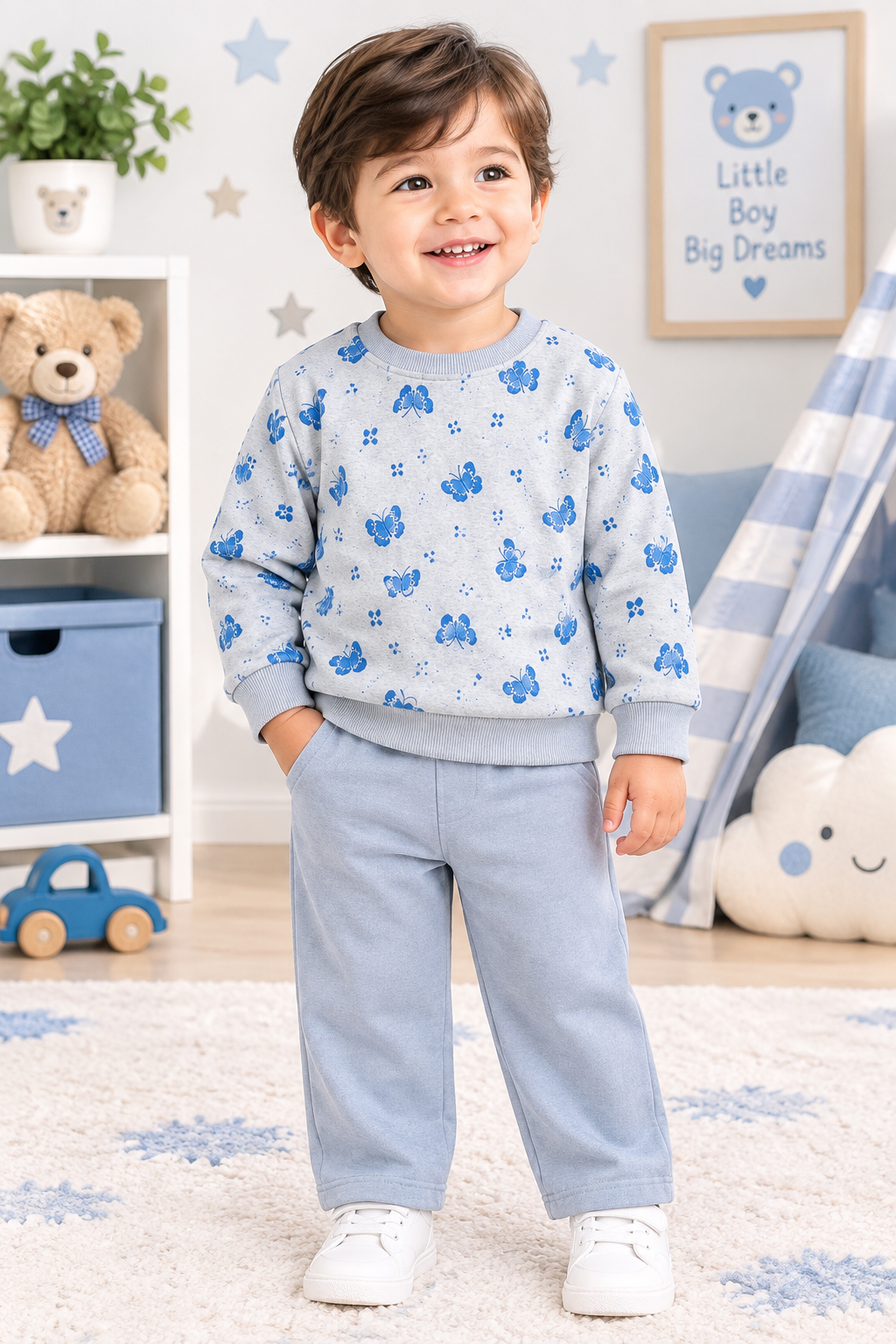 A young child wearing a light blue and white long-sleeve sweatshirt with blue cartoon motifs and matching light blue sweatpants, standing in a decorated children's room.