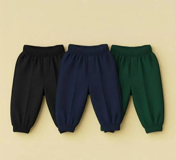 Three pairs of children's elastic-waist jogger pants in black, navy blue, and forest green, arranged side by side on a light beige background.