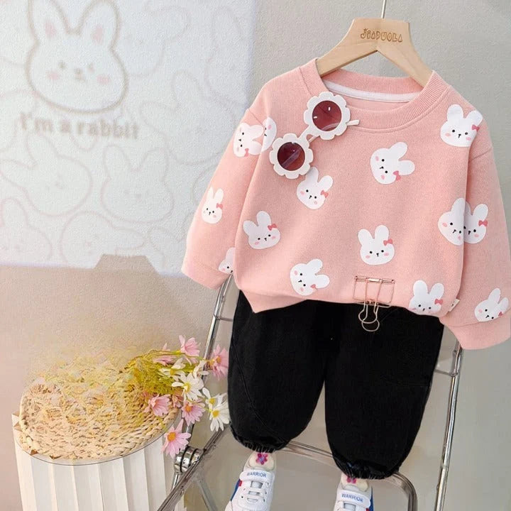 Pink sweater with white bunny patterns on a hanger against a neutral background