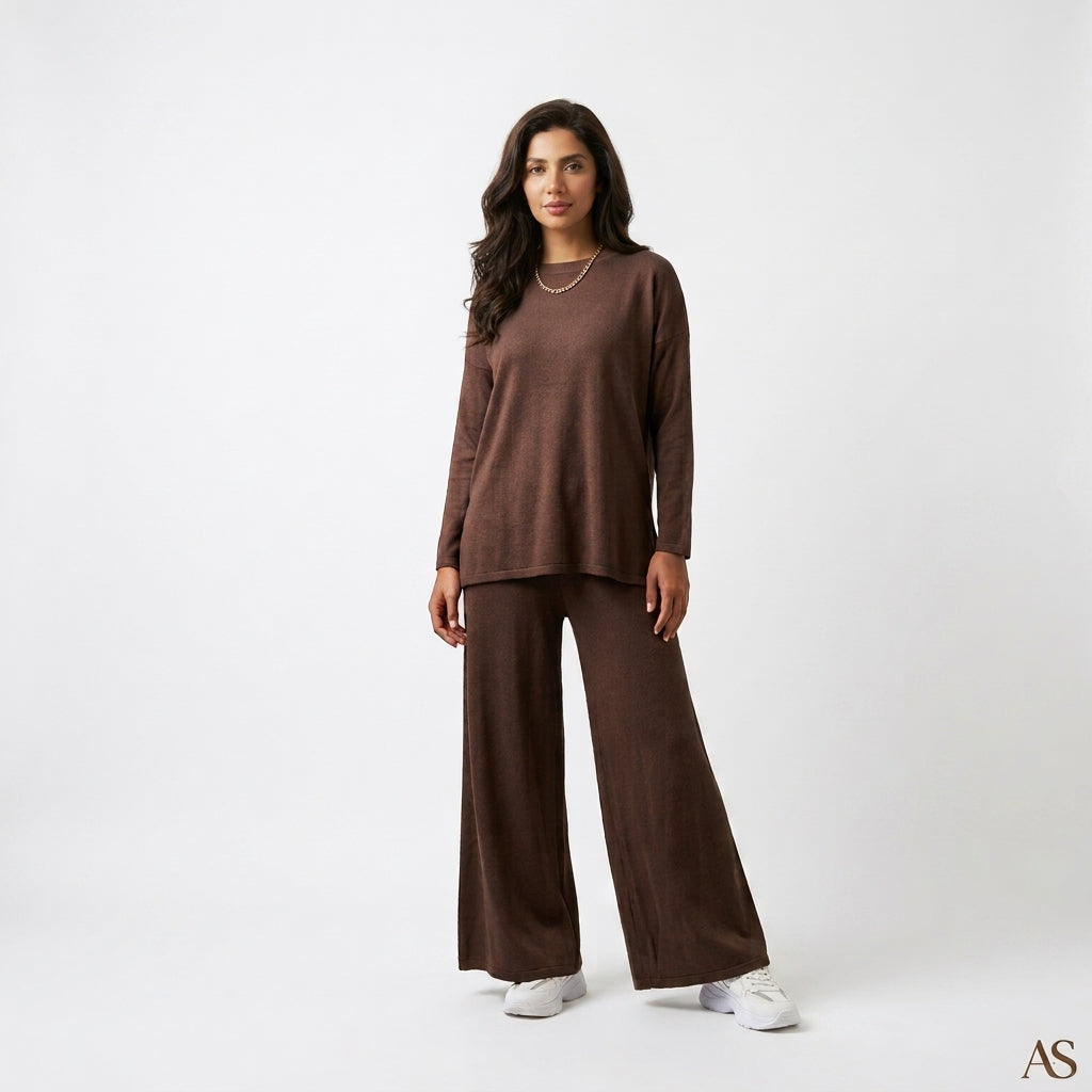 A woman modeling a matching brown lounge set consisting of a long-sleeve top and wide-leg pants, paired with white sneakers against a plain white studio background.