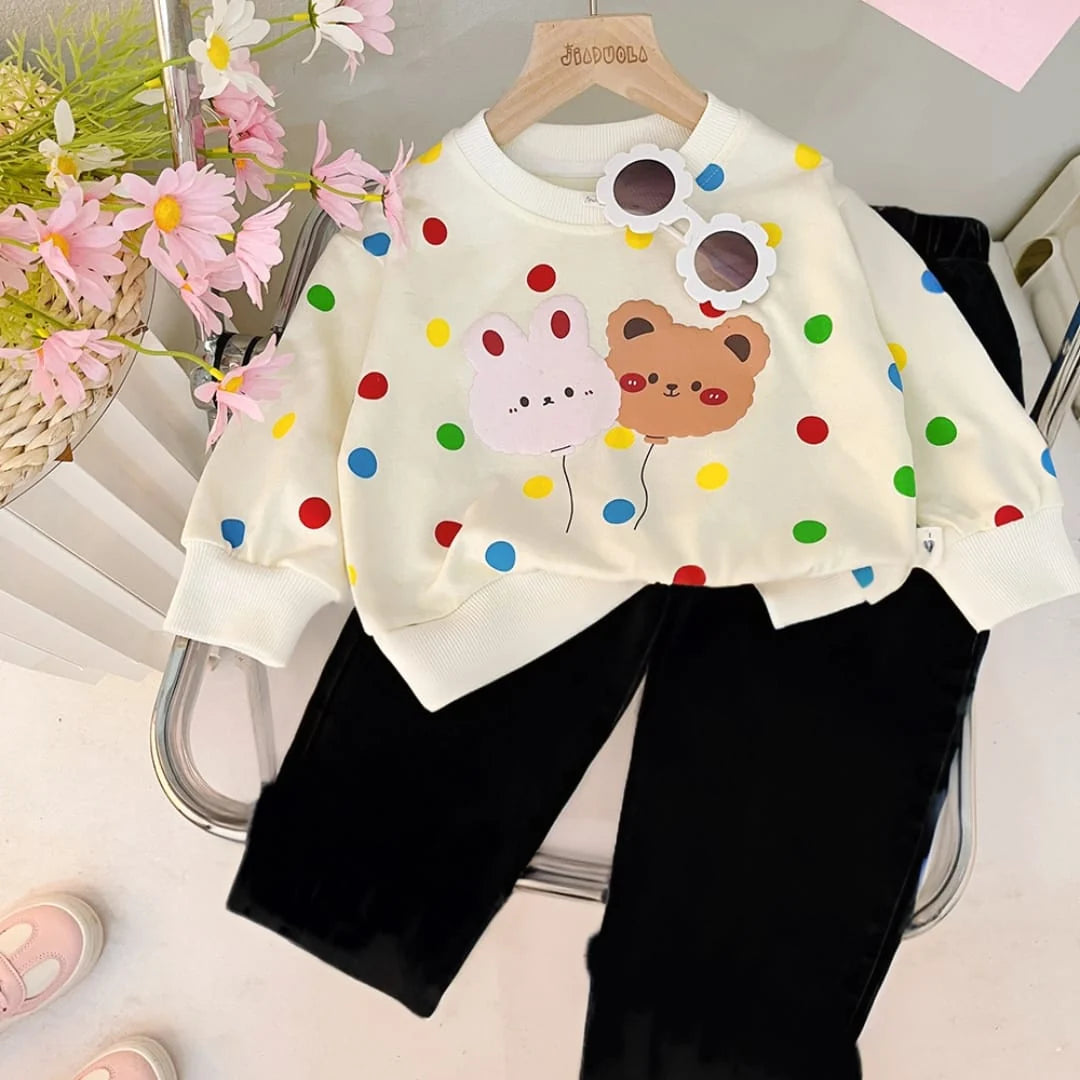 Children's outfit with polka dot shirt featuring cartoon characters and black pants on a white background.