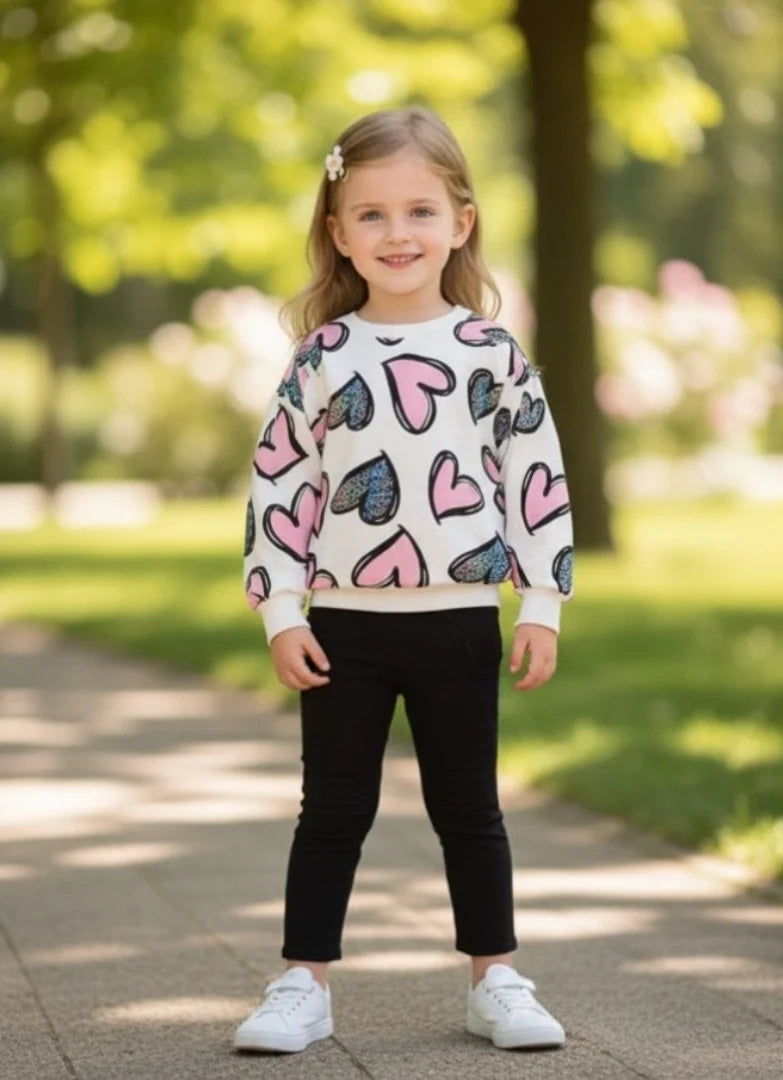 Young girl wearing a sweater with colorful heart patterns outdoors.